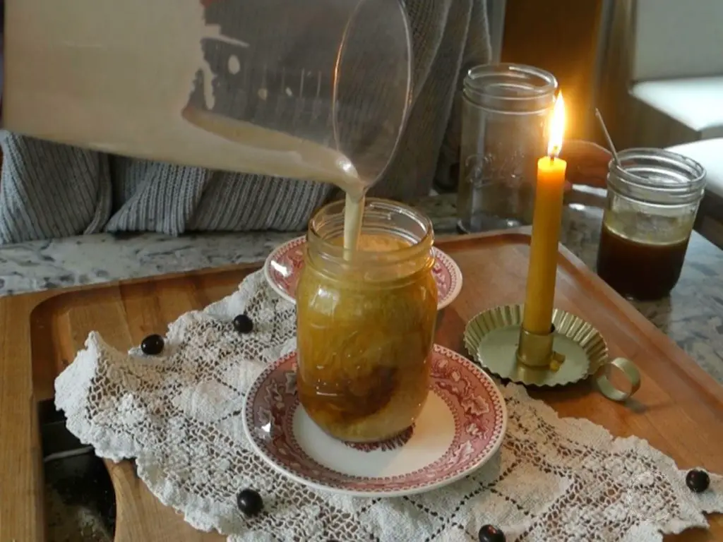 assembling the salted caramel cold foam cold brew in a mason jar pouring the cold foam on top with a candle next to it to set the scene
