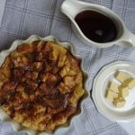 brioche french toast casserole with pads of butter and maple syrup on the side in a flat lay format