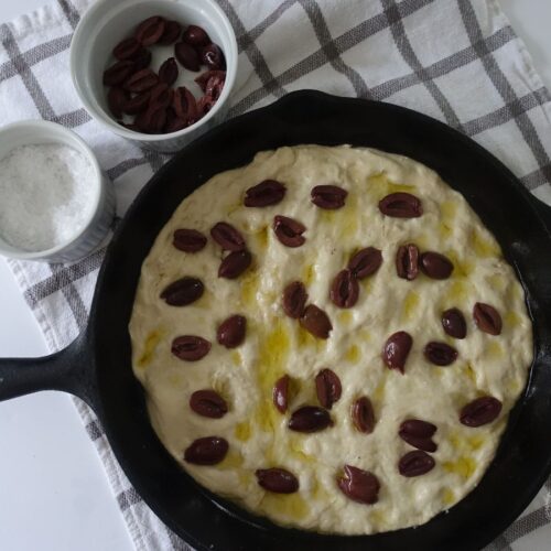 same day sourdough discard focaccia bread unbaked simpled with olive oil and kalamata olives in a cast iron skillet