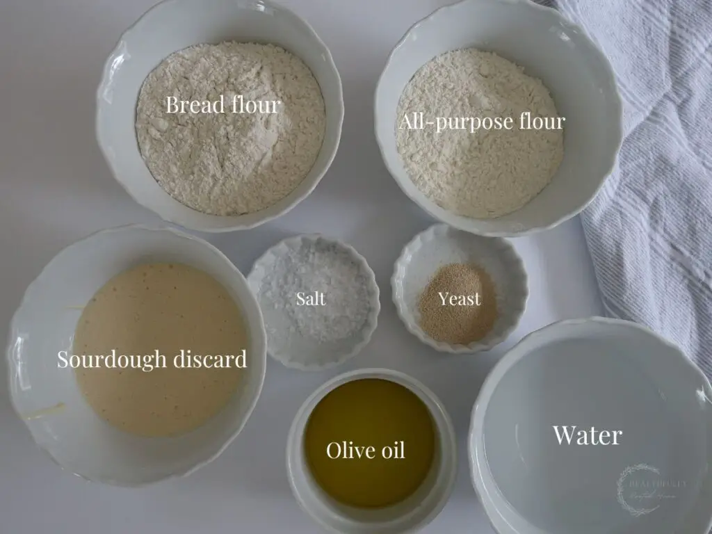 Ingredients for sourdough discard focaccia in white bowls with labels saying what they are