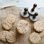 chocolate chip sugar cookies with cookie stamps on a cooling rack with recipes next to it