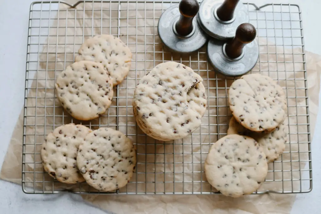 chocolate chip sugar cookies displayed on a wire cooling rack with cookie stamps next to it and a piece of parchment paper underneath