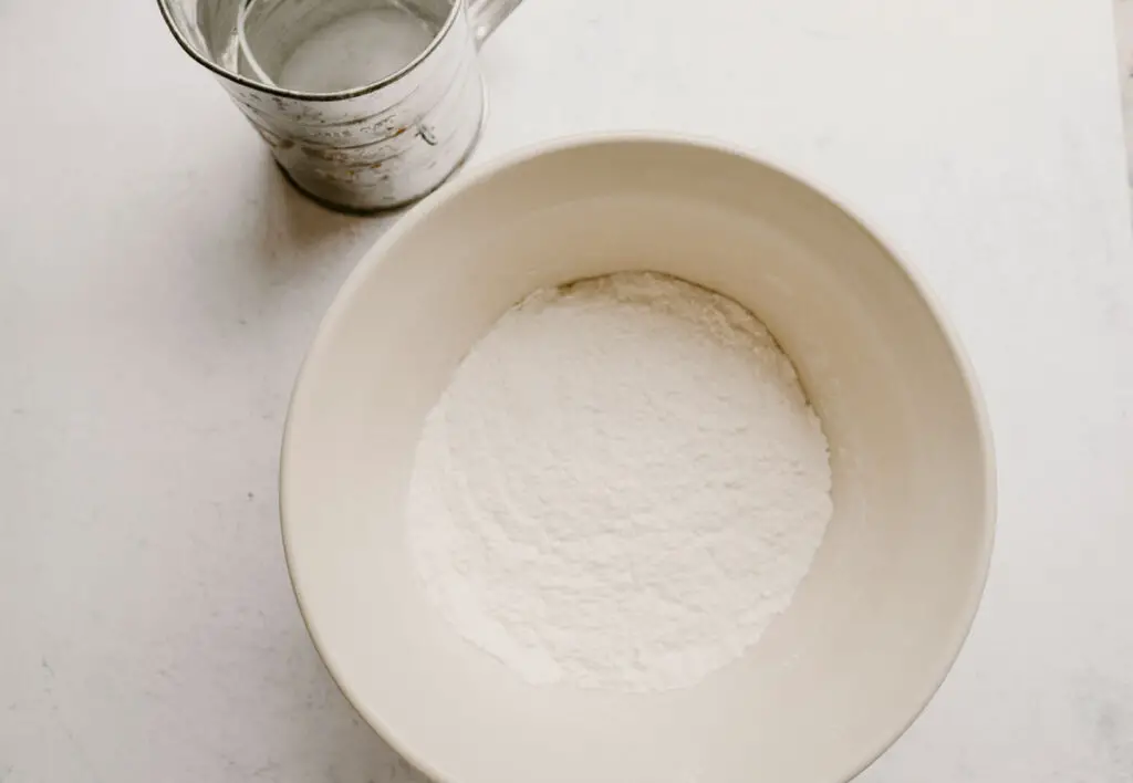 flour, baking soda, cream of tartar whisked together in a bowl with a sifter next to it