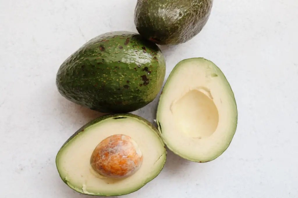 whole avocados with an avocado cut in half on a white background
