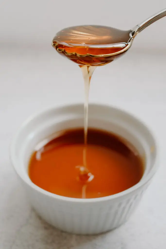 honey drizzling from a spoon into a white bowl of honey