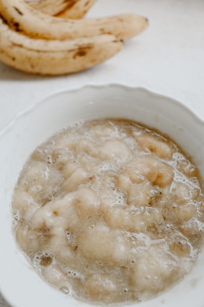 mashed bananas in a white bowl shown as a great applesauce substitue