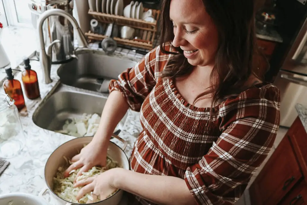 christian homemaker in a plaid dress making homemade sauerkraut smiling joyfully